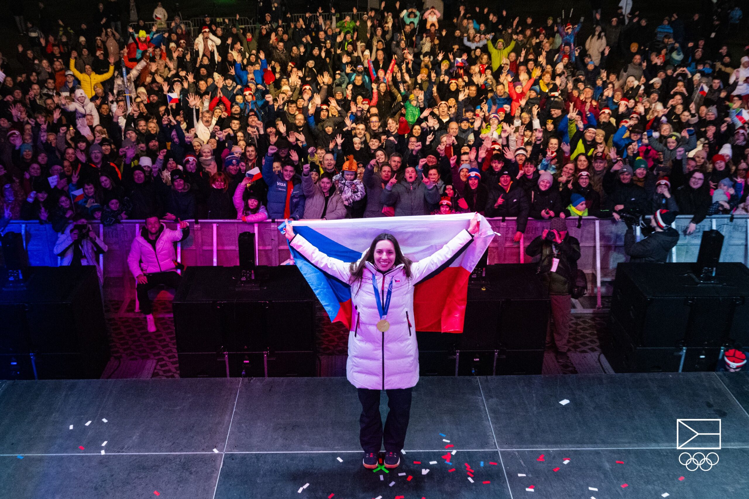 Zuzka Maděrová na pódiu se zlatou medailí a českou vlajkou — fanoušci v pozadí